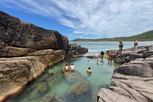 Piscina natural formada entre as pedras da Praia do Rosa Norte, com visitantes na água